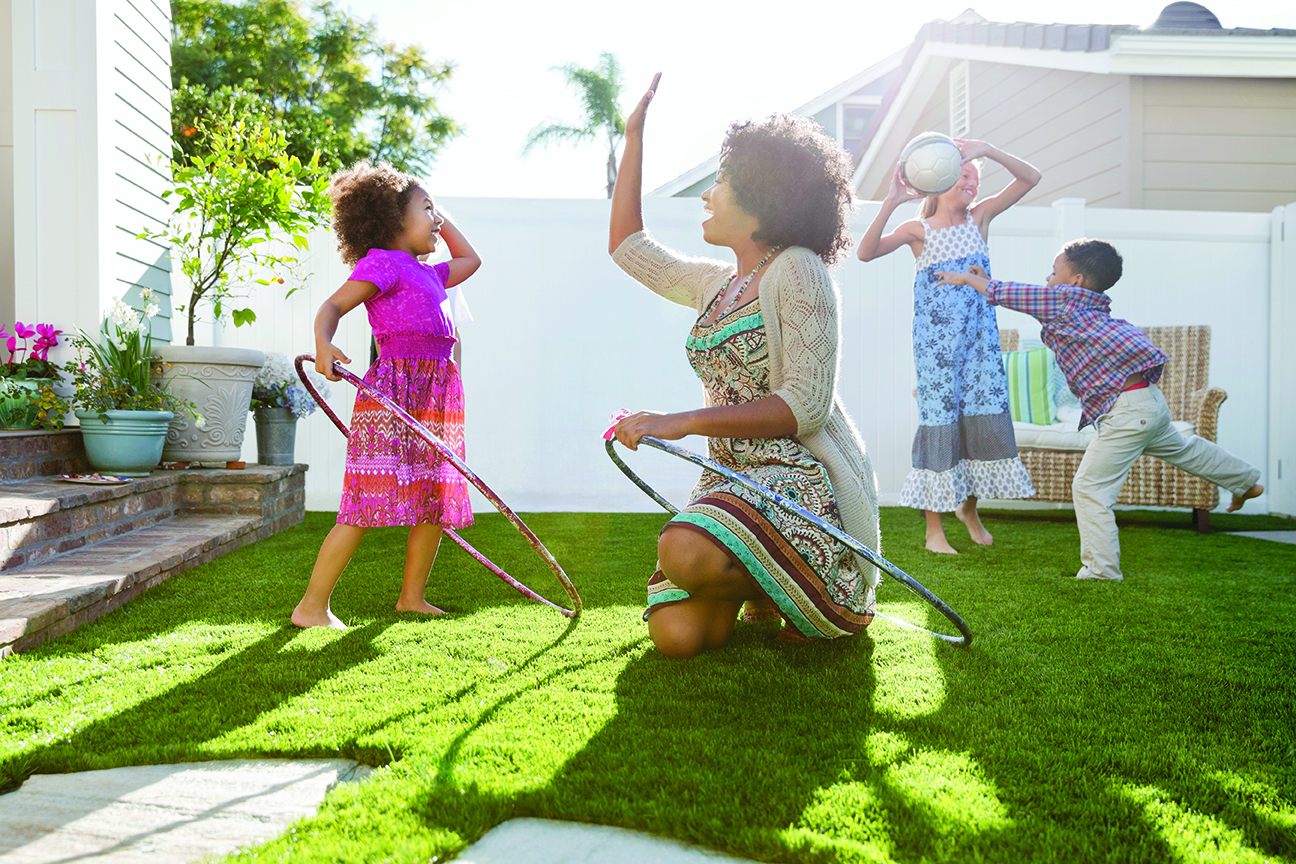 Cheerful mother and daughter with hula hoops giving high five on lawn