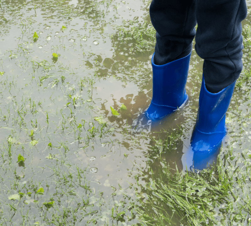 child in blue boot standing in flooded yard
